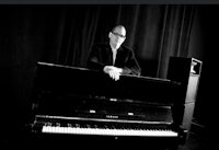 a black and white photo of a man leaning against a piano